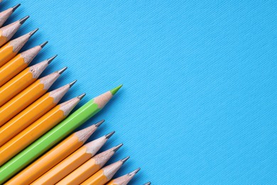 Photo of One green pencil among graphite ones on light blue background, top view. Space for text