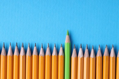 Photo of One green pencil among graphite ones on light blue background, top view. Space for text