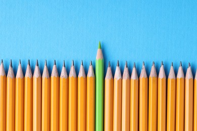 Photo of One green pencil among graphite ones on light blue background, top view. Space for text