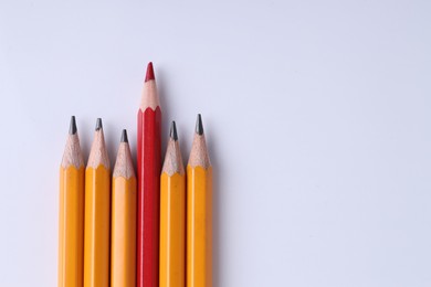 Photo of One red pencil among graphite ones on light grey background, top view. Space for text