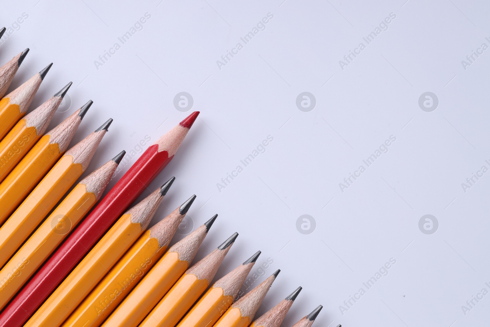 Photo of One red pencil among graphite ones on light grey background, top view. Space for text