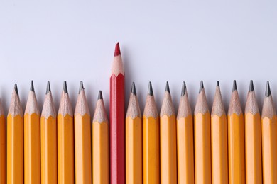 Photo of One red pencil among graphite ones on light grey background, top view