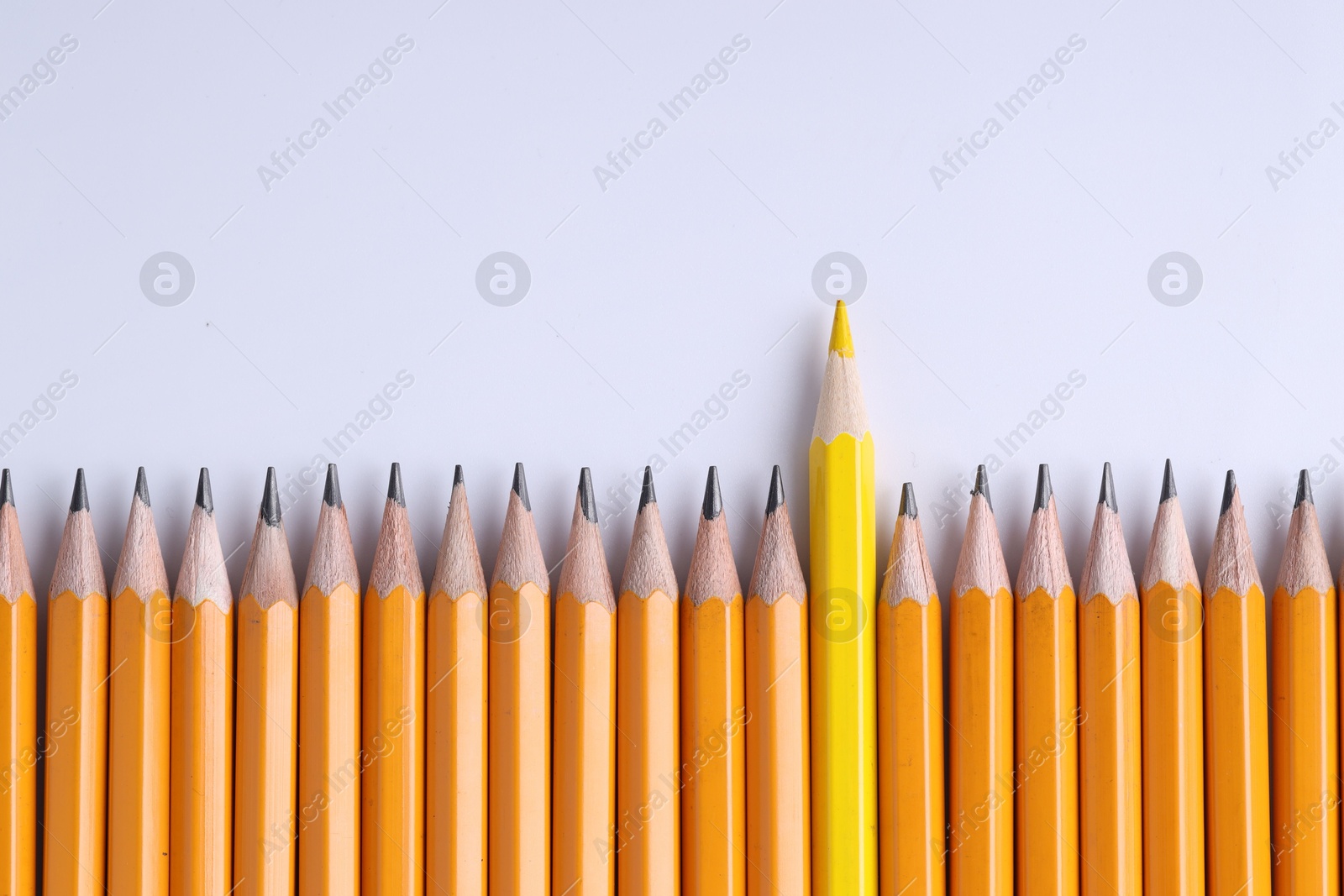 Photo of One yellow pencil among graphite ones on light grey background, top view. Space for text