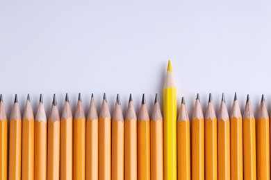 Photo of One yellow pencil among graphite ones on light grey background, top view. Space for text