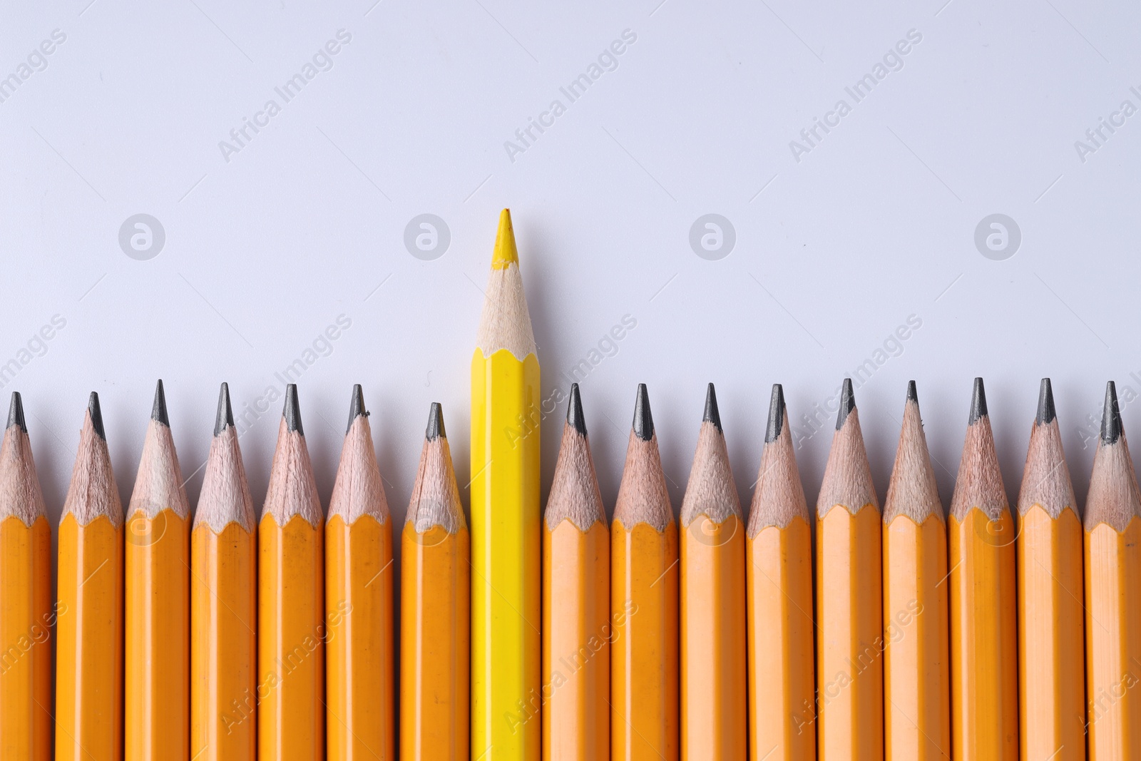 Photo of One yellow pencil among graphite ones on light grey background, top view