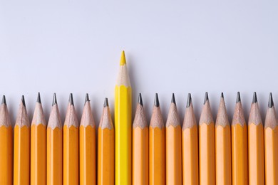 One yellow pencil among graphite ones on light grey background, top view