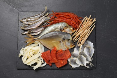 Many different dried fish snacks on black table, top view