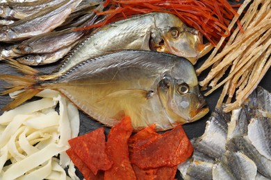 Many different dried fish snacks on black table, closeup