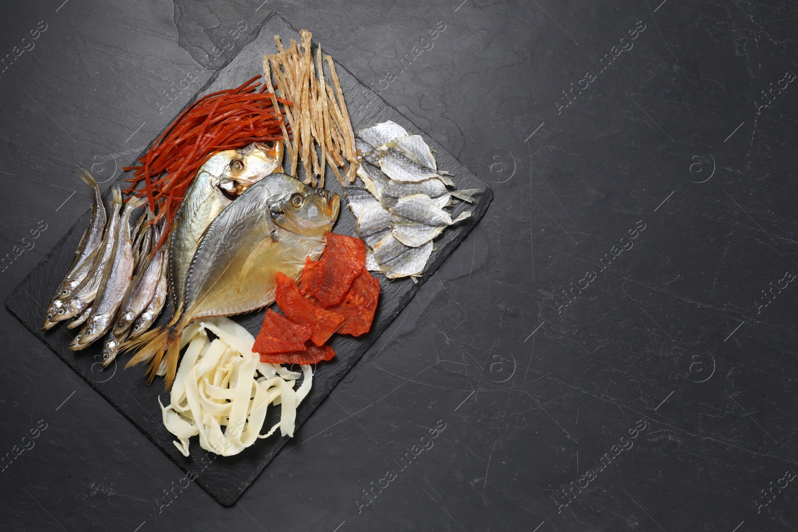 Photo of Many different dried fish snacks on black table, top view. Space for text