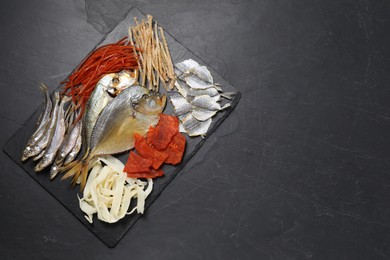 Photo of Many different dried fish snacks on black table, top view. Space for text