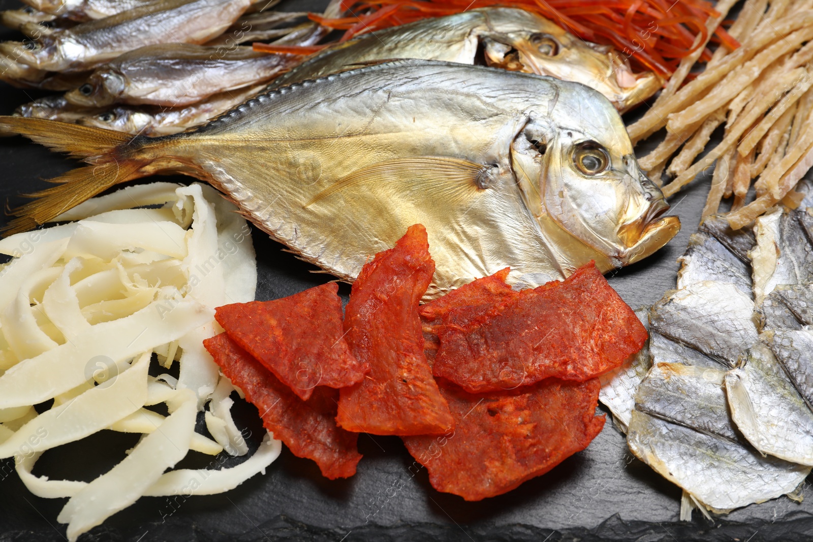 Photo of Many different dried fish snacks on black table, closeup