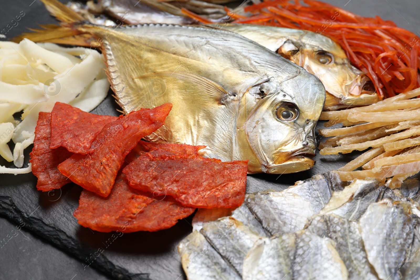 Photo of Many different dried fish snacks on black table, closeup