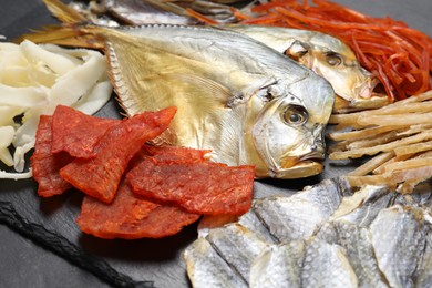 Many different dried fish snacks on black table, closeup