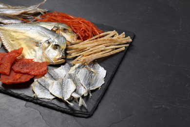 Many different dried fish snacks on black table. Space for text