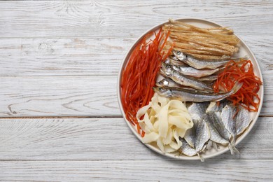 Many different dried fish snacks on white wooden table, top view. Space for text