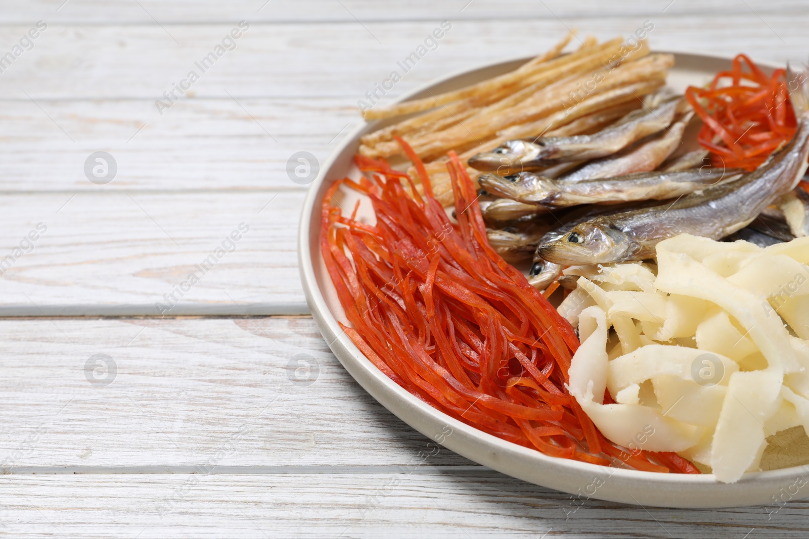 Photo of Many different dried fish snacks on white wooden table. Space for text