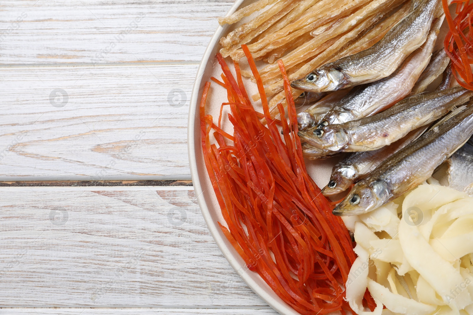 Photo of Many different dried fish snacks on white wooden table, top view. Space for text