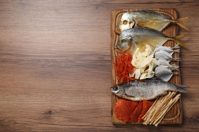 Many different dried fish snacks on wooden table, top view. Space for text