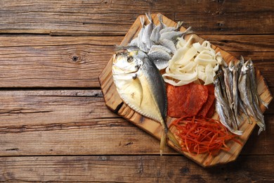 Photo of Many different dried fish snacks on wooden table, top view. Space for text