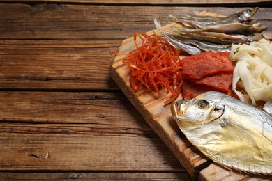 Many different dried fish snacks on wooden table. Space for text