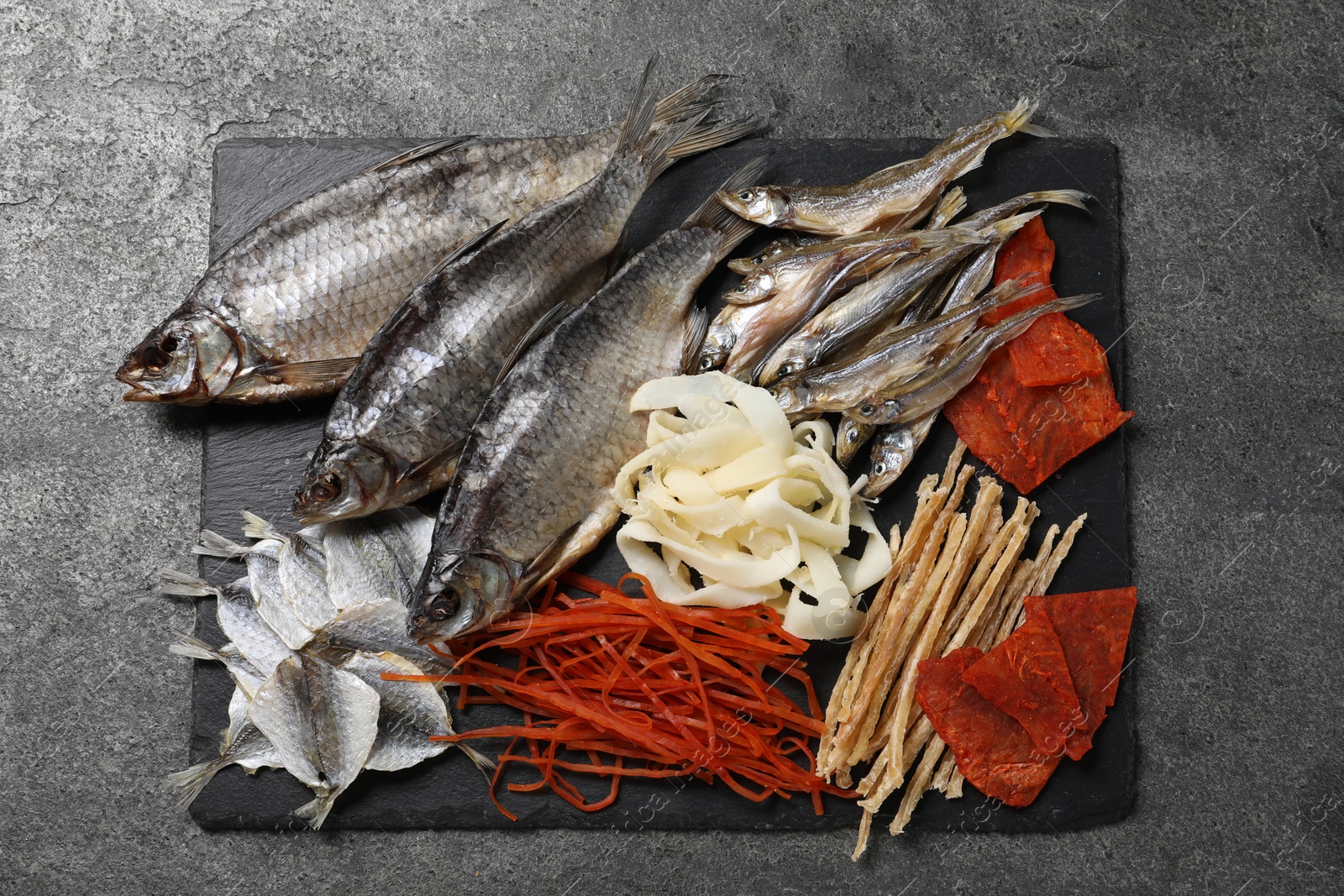 Photo of Many different dried fish snacks on grey table, top view