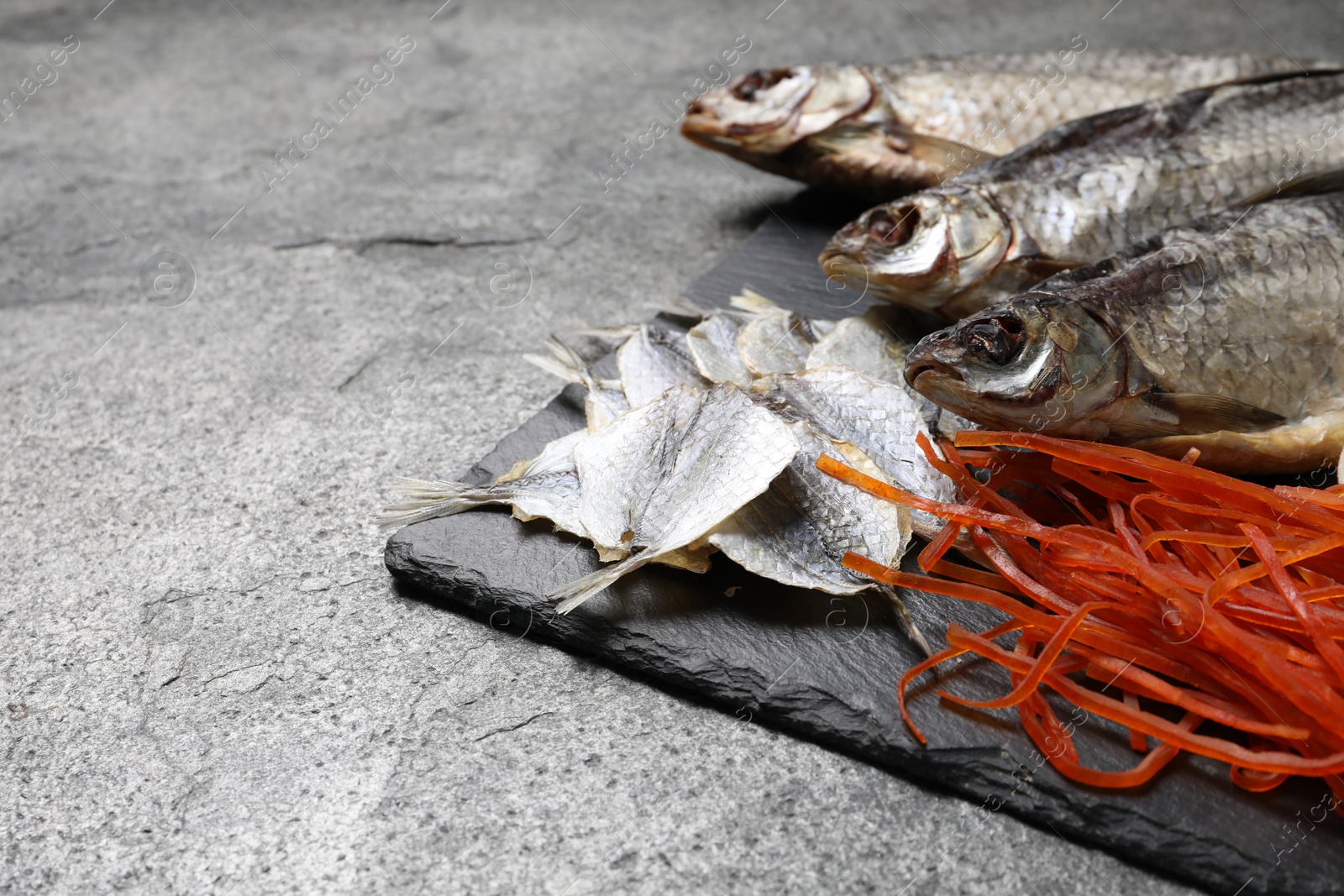 Photo of Many different dried fish snacks on grey table, closeup. Space for text