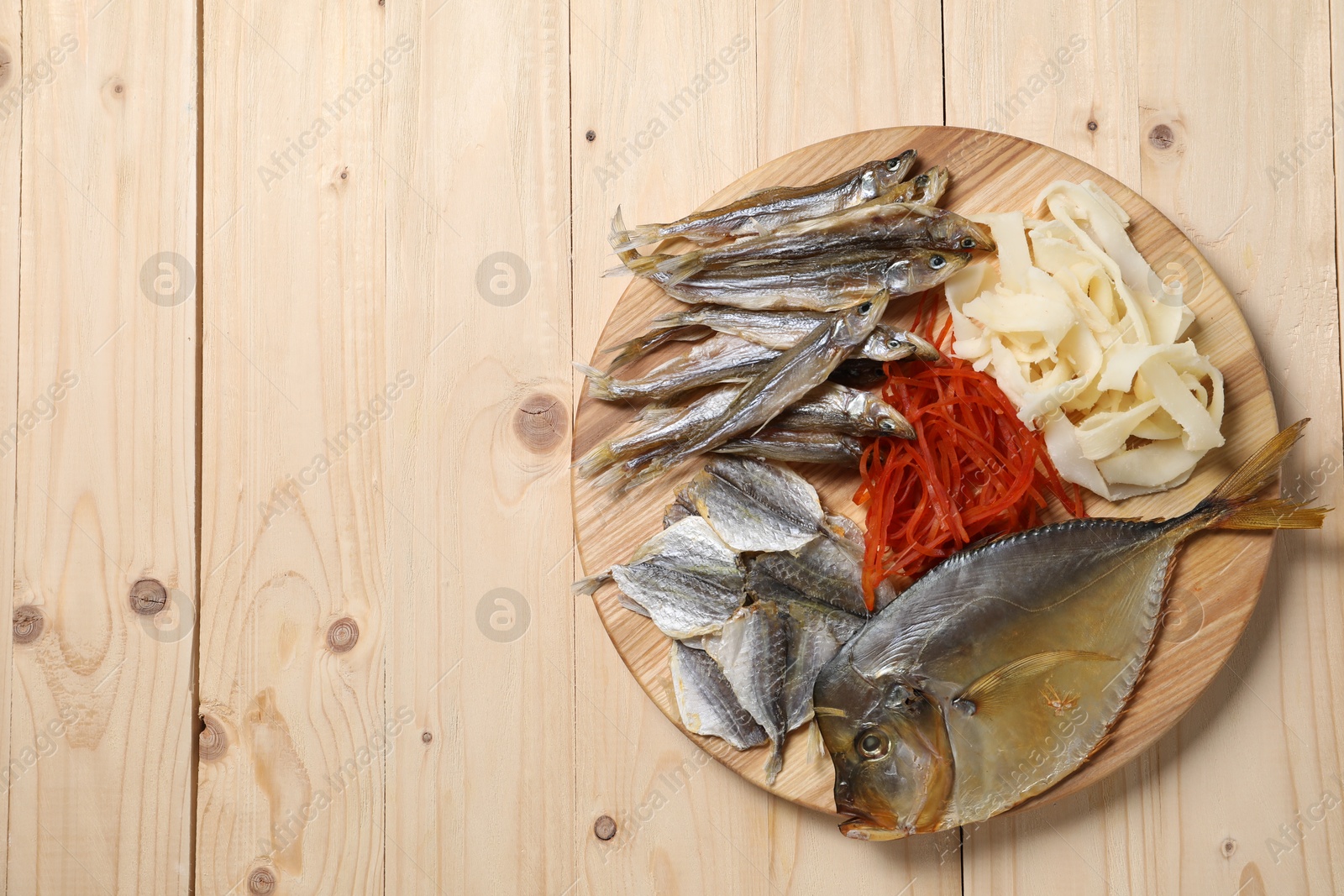 Photo of Many different dried fish snacks on wooden table, top view. Space for text