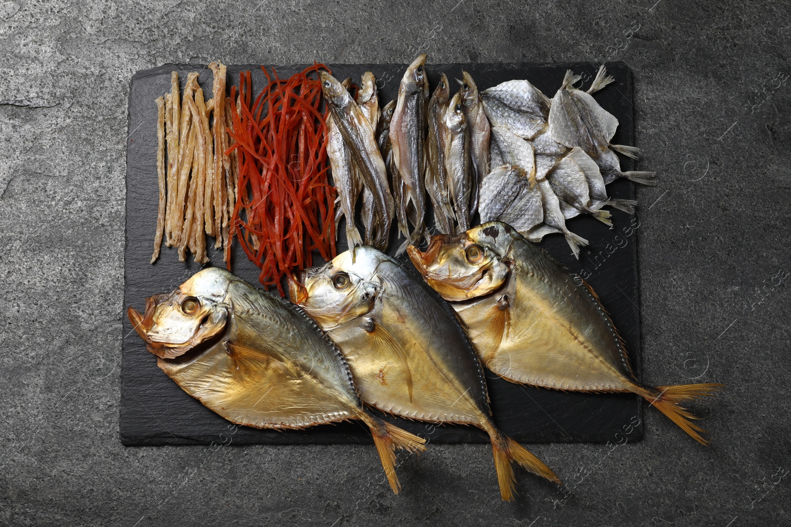 Photo of Many different dried fish snacks on grey table, top view