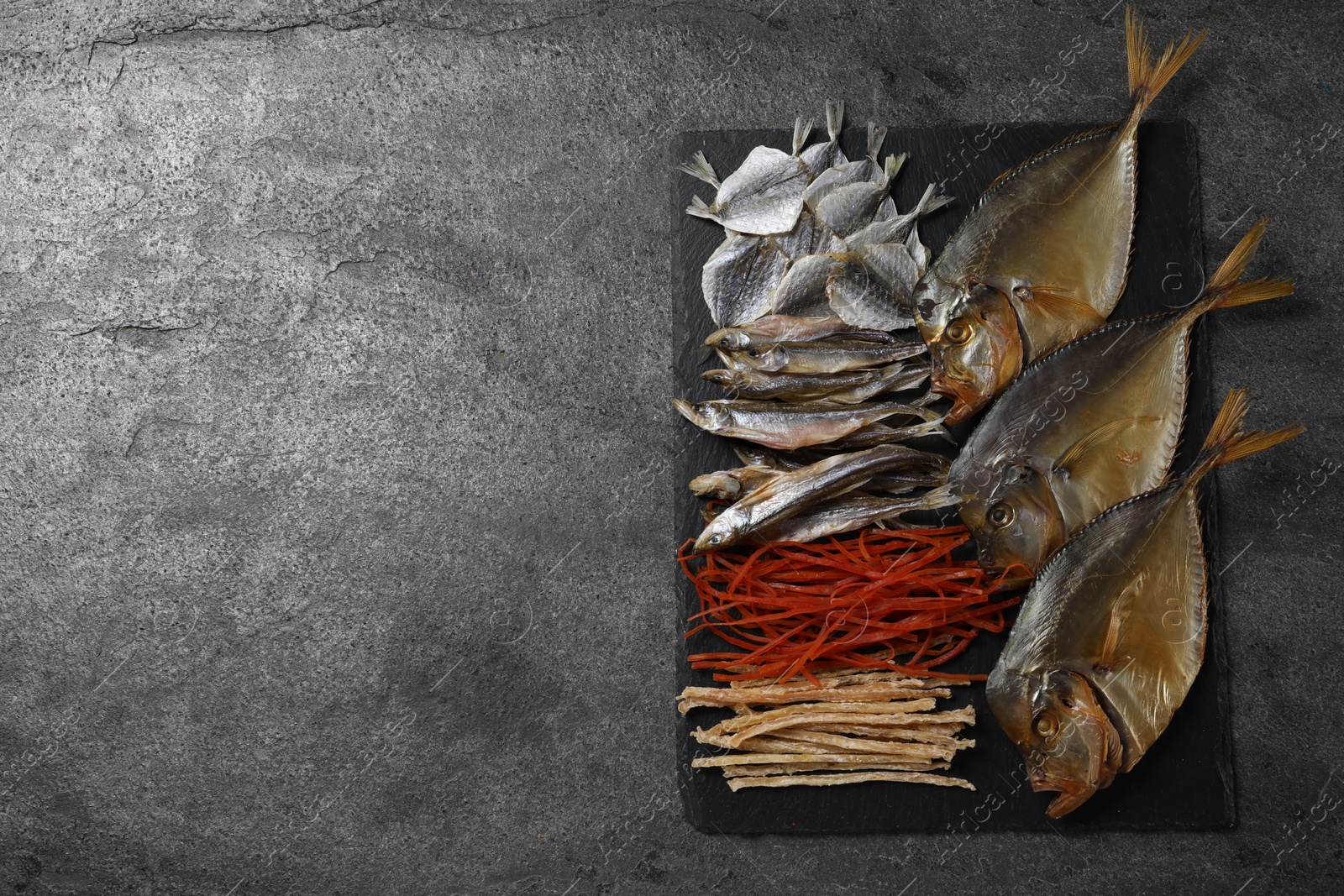 Photo of Many different dried fish snacks on grey table, top view. Space for text