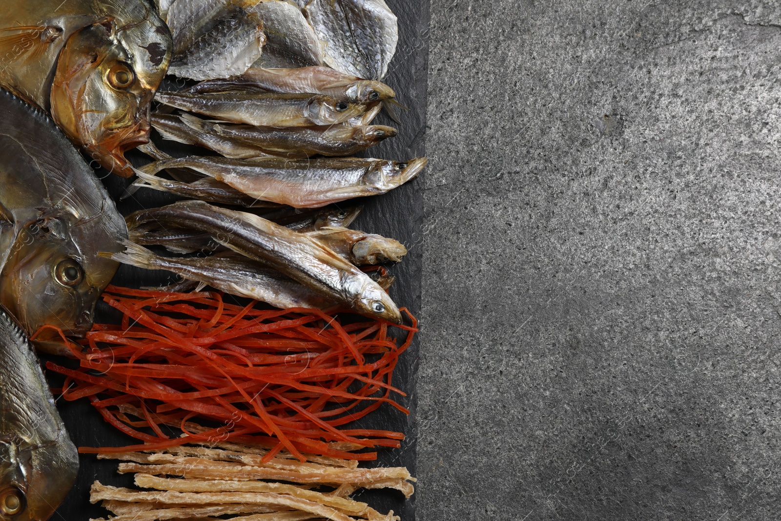 Photo of Many different dried fish snacks on grey table, top view. Space for text