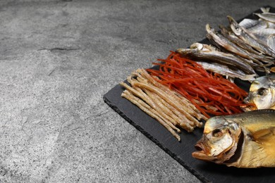 Many different dried fish snacks on grey table, closeup. Space for text