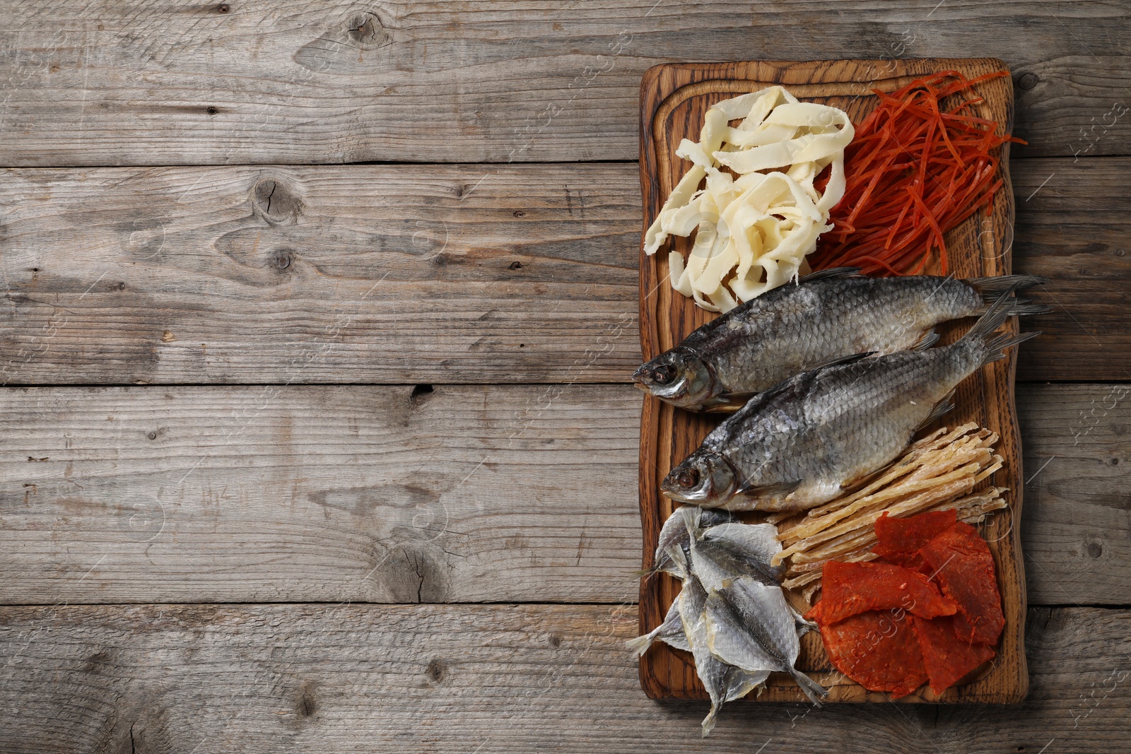 Photo of Many different dried fish snacks on wooden table, top view. Space for text