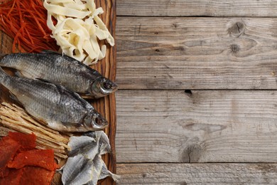 Many different dried fish snacks on wooden table, top view. Space for text