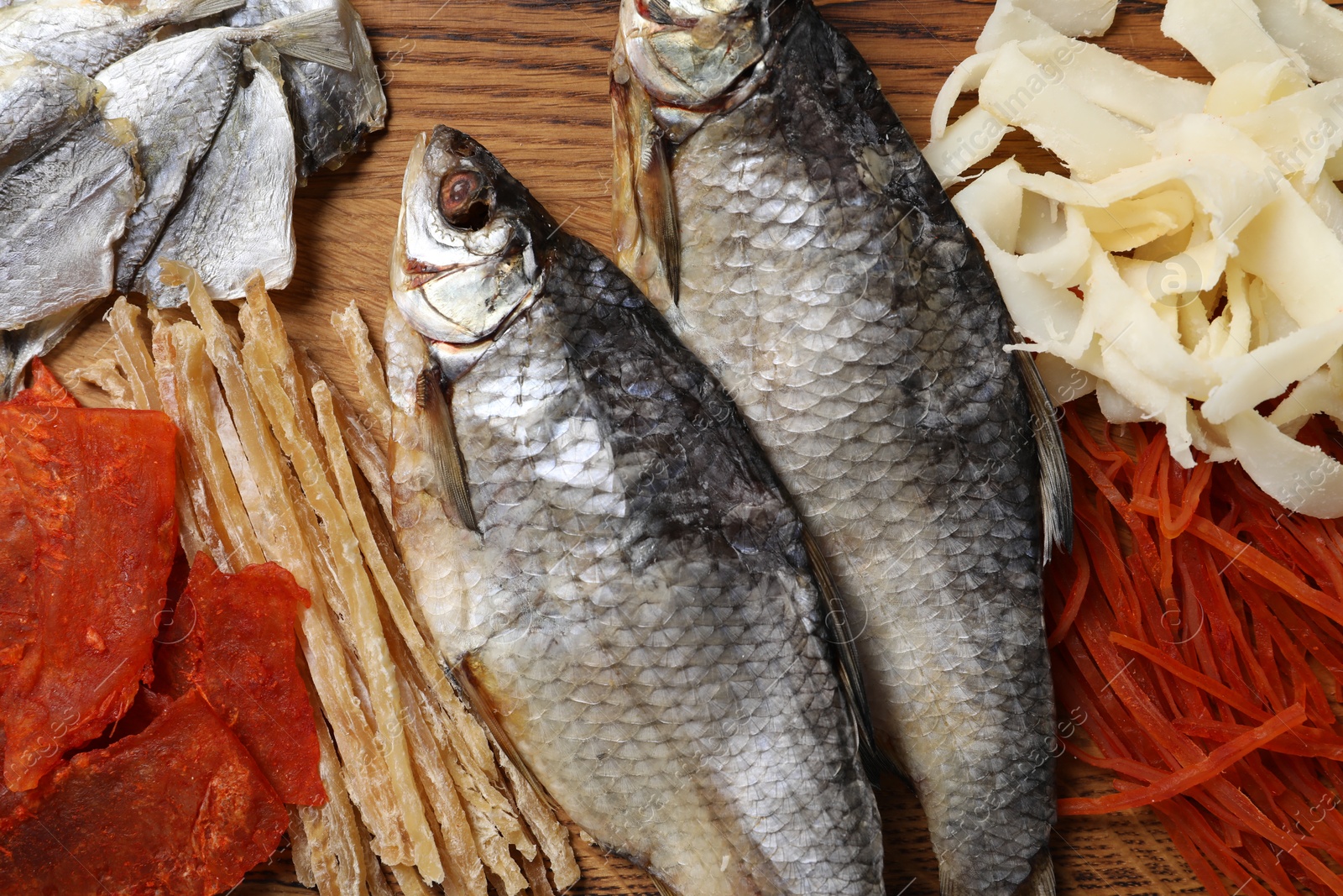 Photo of Many different dried fish snacks on wooden table, closeup