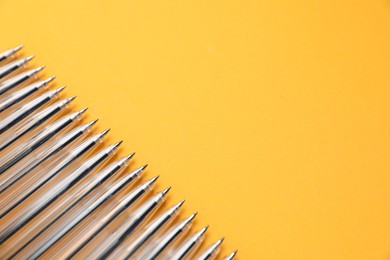 Photo of Many ballpoint pens on orange background, above view. Space for text