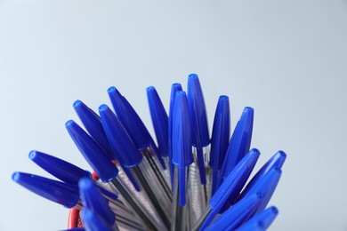 Photo of Many ballpoint pens in holder on light grey background, closeup