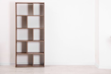 Photo of Empty wooden shelving unit near white wall indoors, space for text