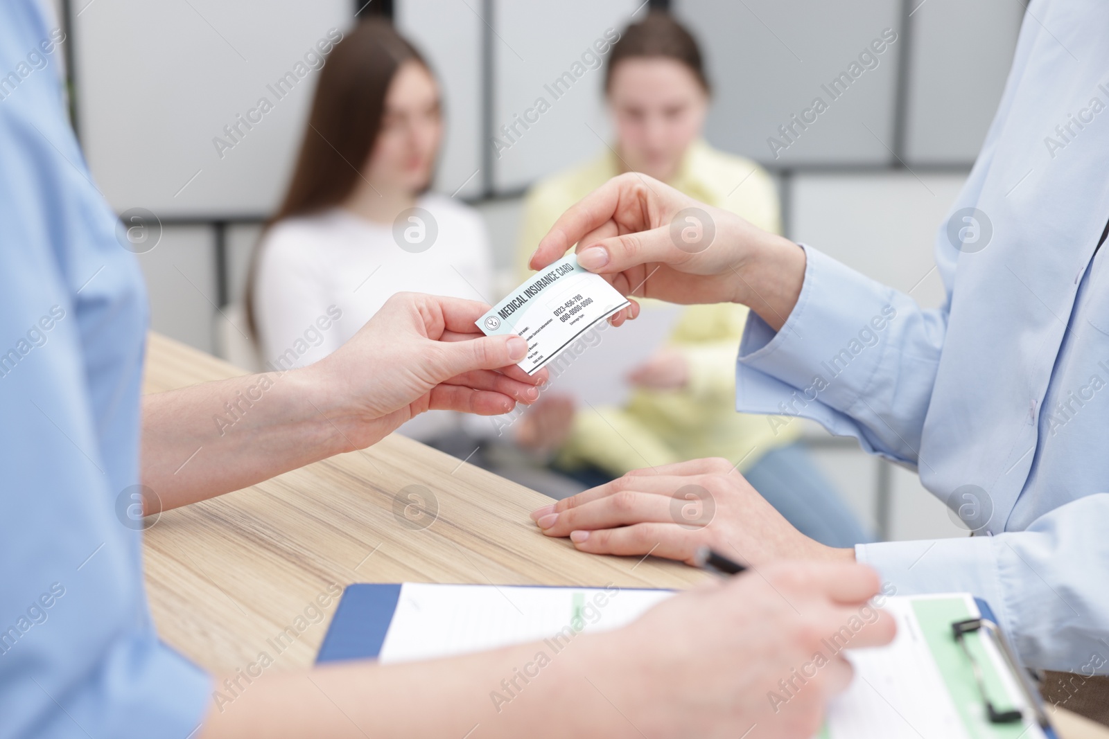 Photo of Patient giving medical insurance card to receptionist at wooden counter in clinic, closeup