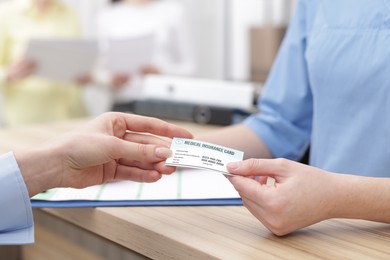 Patient giving medical insurance card to receptionist at wooden counter in clinic, closeup