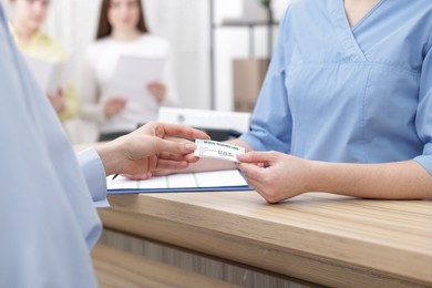 Photo of Patient giving medical insurance card to receptionist at wooden counter in clinic, closeup