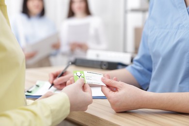 Photo of Patient giving medical insurance card to receptionist at wooden counter in clinic, closeup