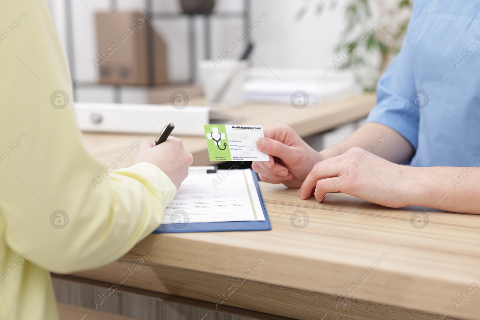 Photo of Patient filling document and receptionist with medical insurance card at wooden counter in clinic, closeup