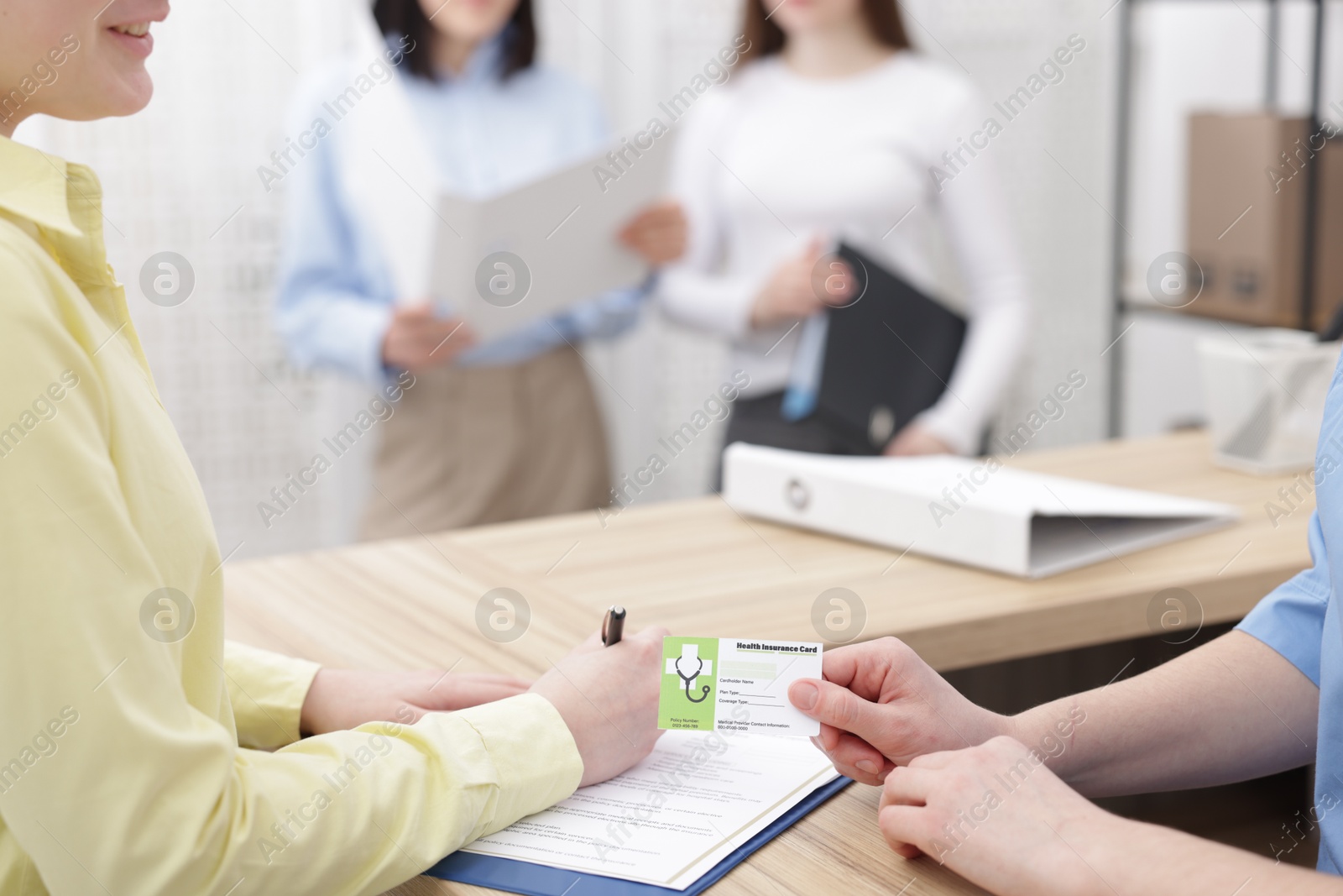 Photo of Patient filling document and receptionist with medical insurance card at wooden counter in clinic, closeup