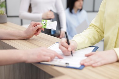 Photo of Patient filling document and receptionist with medical insurance card at wooden counter in clinic, closeup