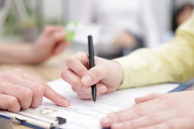 Photo of Patient filling document and receptionist with medical insurance card at counter in clinic, closeup