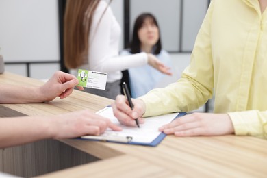 Patient filling document and receptionist with medical insurance card at wooden counter in clinic, closeup