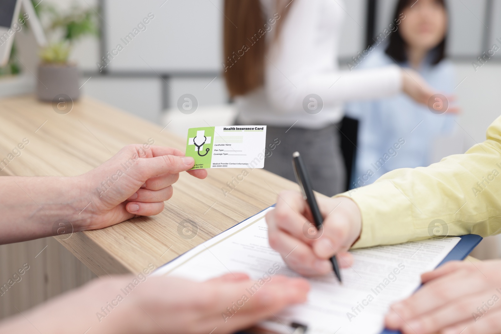 Photo of Patient filling document and receptionist with medical insurance card at wooden counter in clinic, closeup