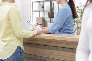 Photo of Patient with medical insurance card and receptionist filling document at wooden counter in clinic, closeup