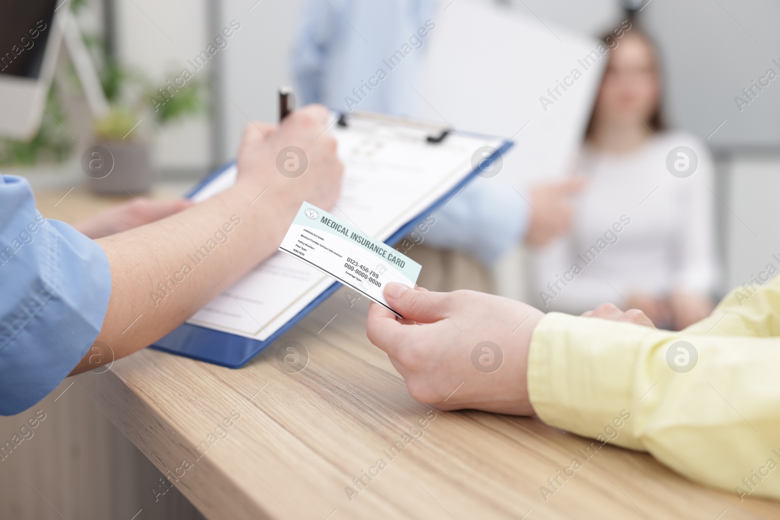 Photo of Patient with medical insurance card and receptionist filling document at wooden counter in clinic, closeup