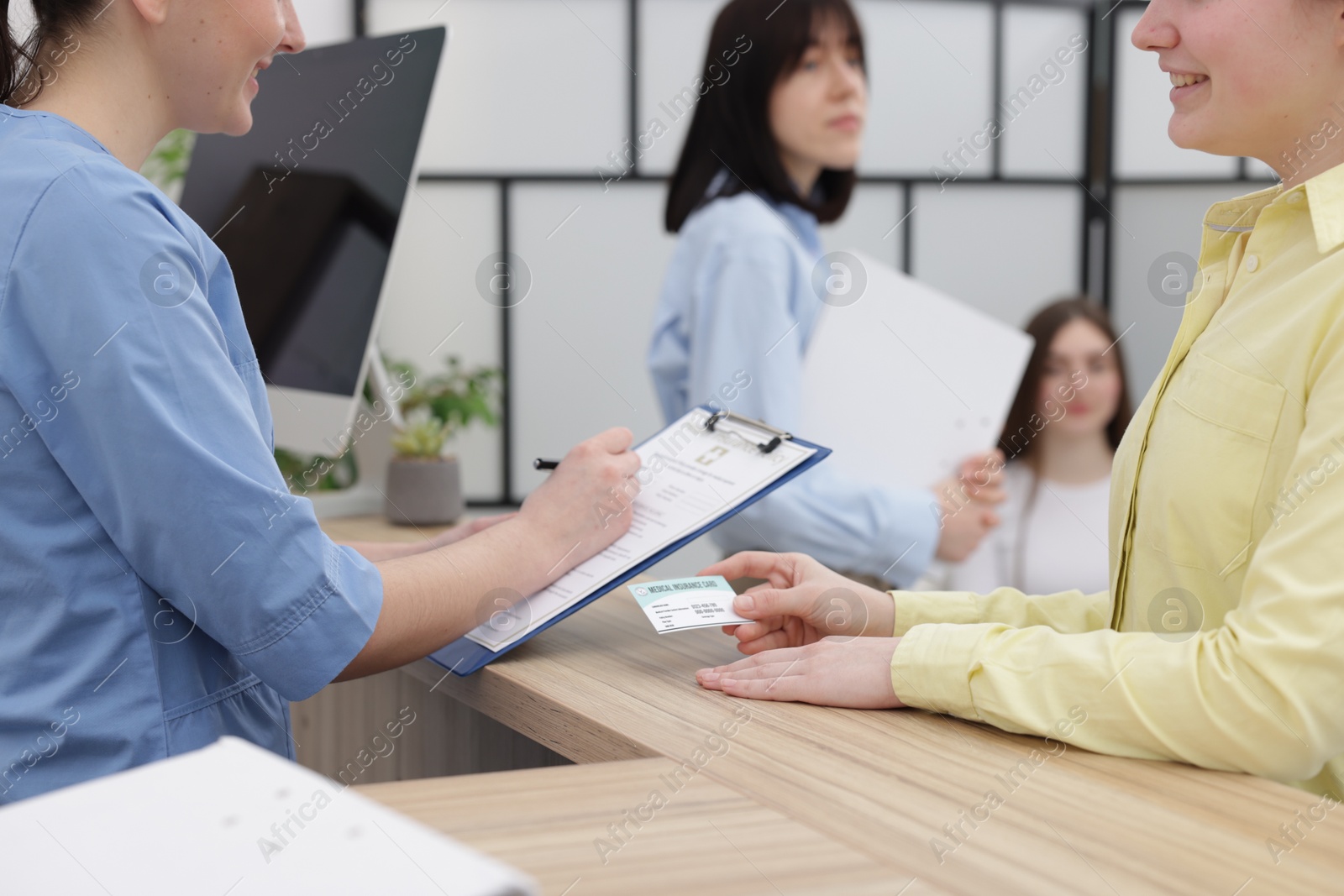 Photo of Patient with medical insurance card and receptionist filling document at wooden counter in clinic, closeup